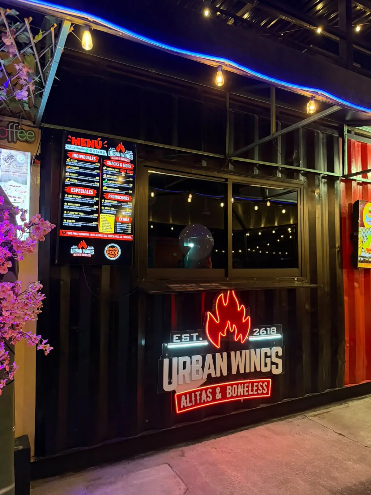 Contenedor negro de Urban Wings con su letrero de neón y el menú en la ventana